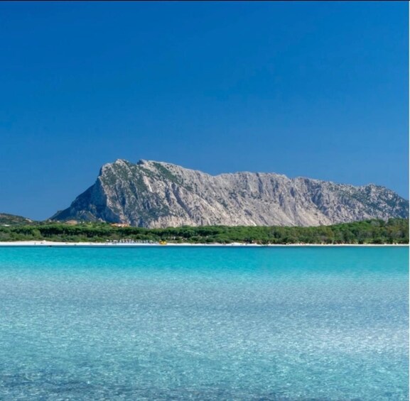 A clear blue sea with a rocky mountain in the background. 1