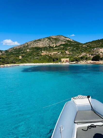 A boat on clear turquoise water with a rocky coastline and a hill in the background. 2