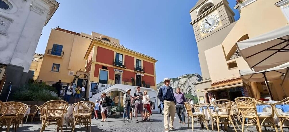 A cobblestone street with outdoor seating, a clock tower, and a building with a sign. 3