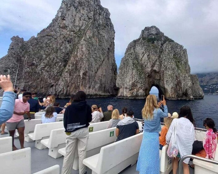 A boat tour with passengers observing rocky formations and a sea arch. 1