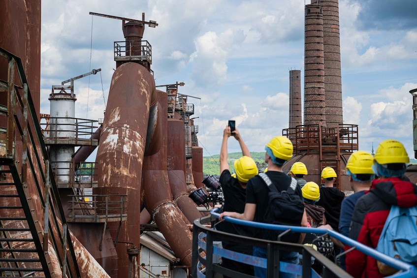 Industrial structures, a person taking a photo, and people in safety helmets. 1