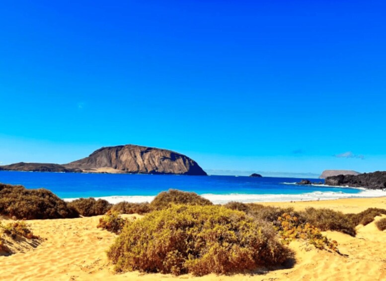 A coastal landscape with a prominent rock formation, sandy beach, and sparse vegetation. 5