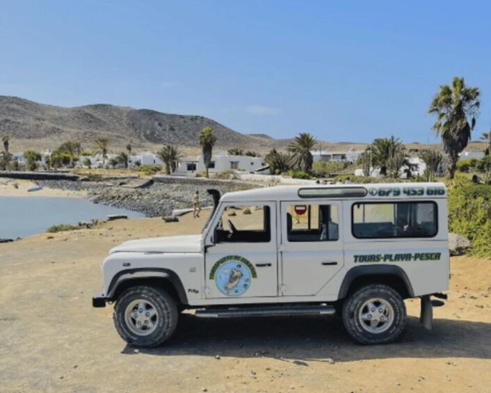 A white off-road vehicle parked on a sandy beach with a coastal landscape in the background. 3