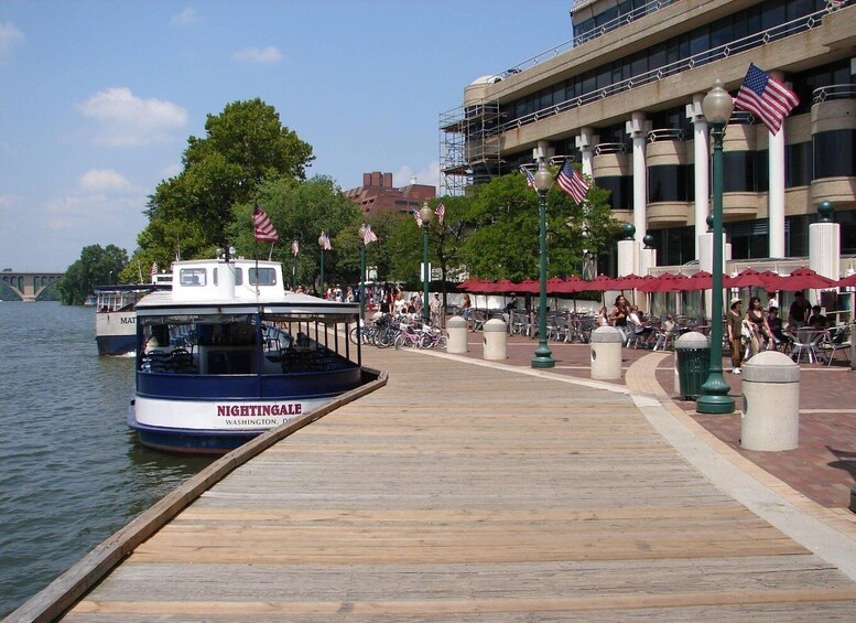 A wooden dock with a boat named 'NIGHTINGALE' docked at the end. There are American flags and a building with a balcony in the background. 4