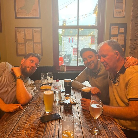 Three people sitting at a wooden table with drinks, a smartphone, and a window view of a street. 3