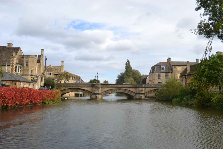 A stone bridge over a calm river, surrounded by historic buildings and autumn foliage. 1