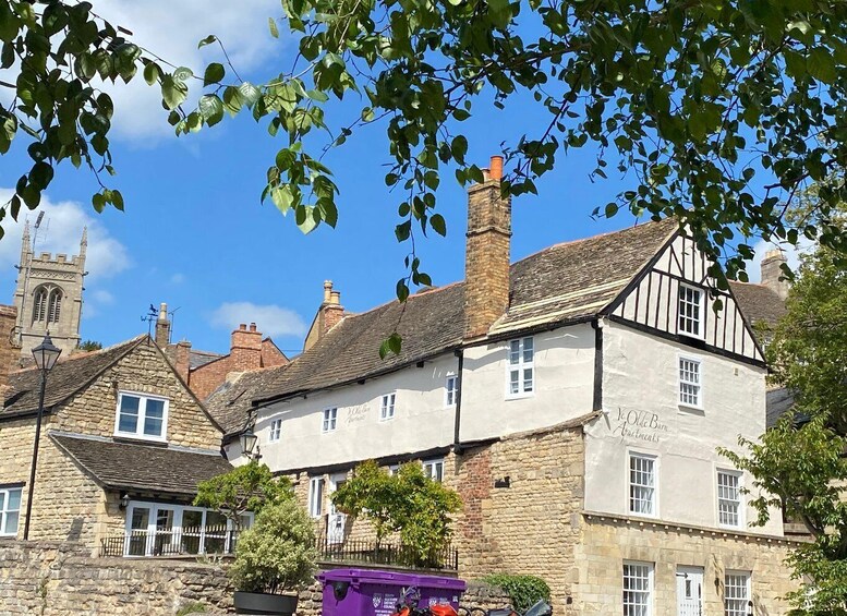 A traditional stone building with a Tudor-style half-timbered facade, a church steeple, and a clear blue sky. 3