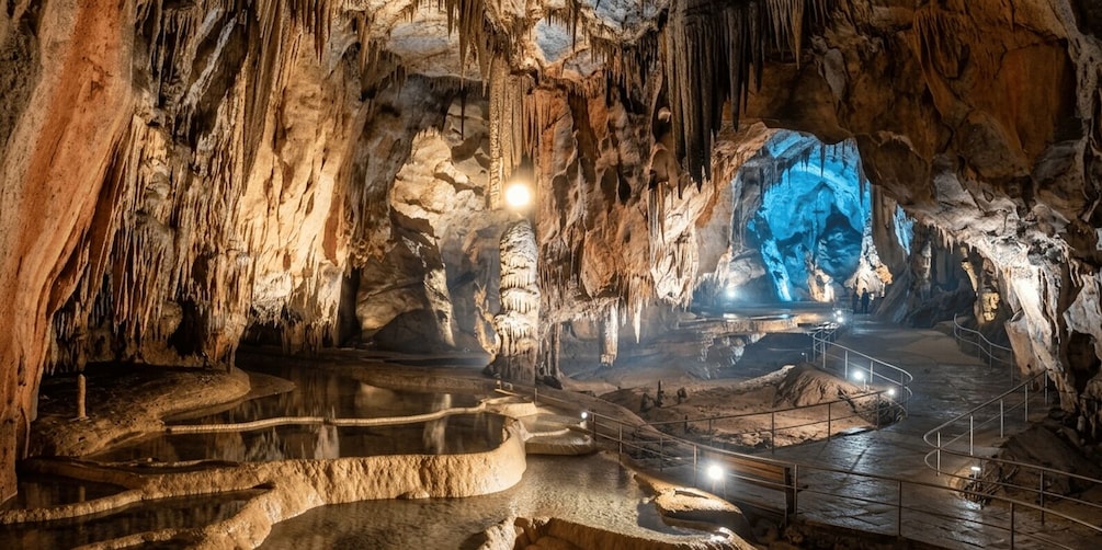 A cave with stalactites, a water pool, and a blue-lit cavern. 1