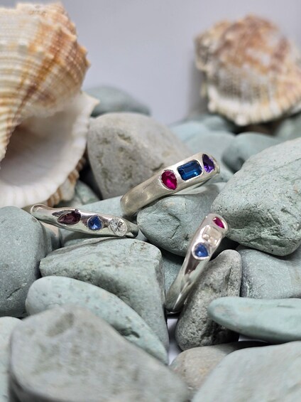 Two silver rings with blue and pink gemstones on a bed of smooth, light-colored stones. 4