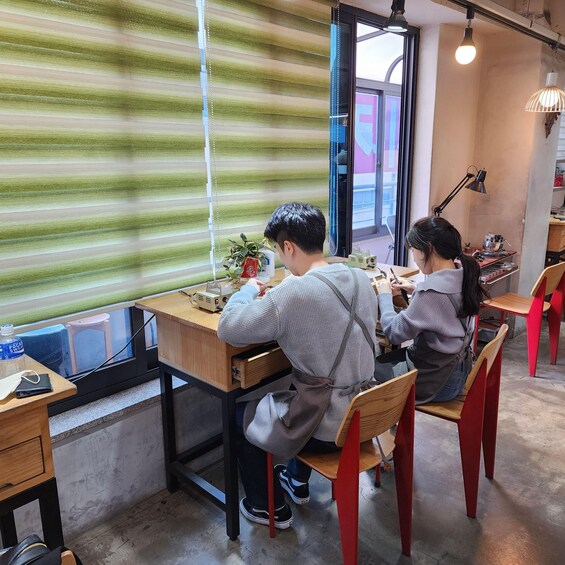 Two people seated at a wooden table with a laptop, a plant, and a water bottle. 1