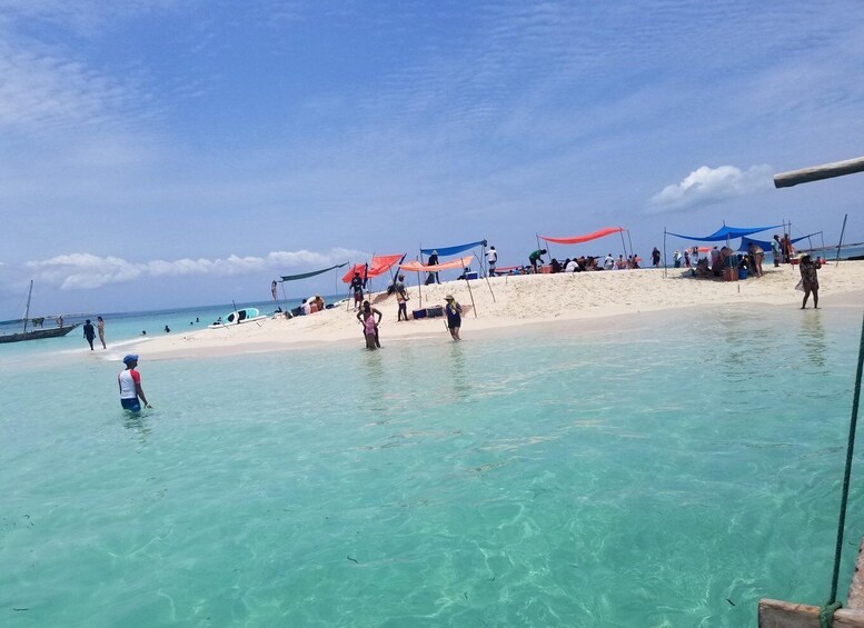 A beach with clear turquoise water, people walking and standing, and colorful beach umbrellas. 4