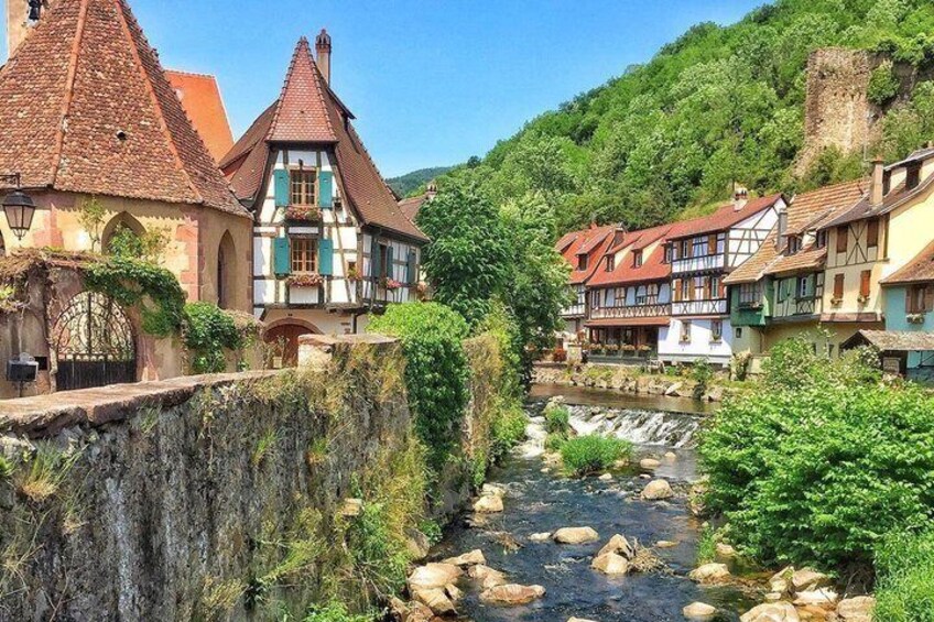 A river flowing through a town with traditional half-timbered houses and a castle on a hill. 2