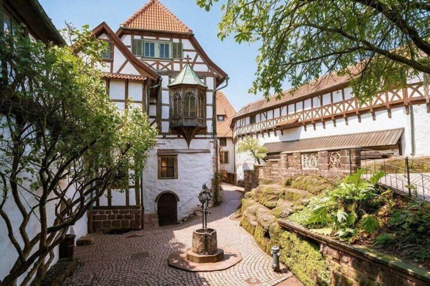 A courtyard with a white building, a tower, and a stone wall with greenery. 5