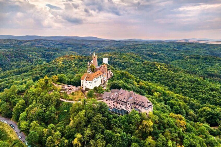 A castle surrounded by dense forest, a road, and a cloudy sky. 2