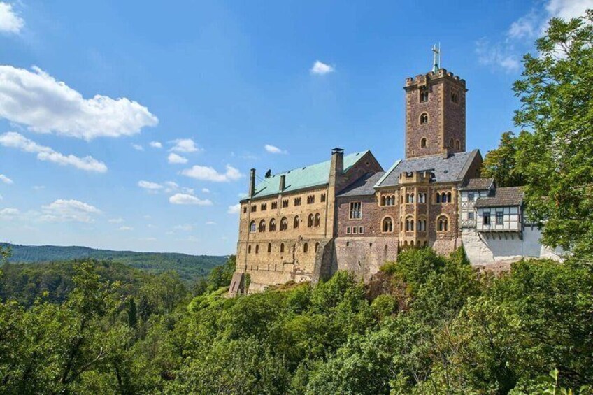 A historic castle with a prominent tower, surrounded by lush greenery and a clear blue sky. 1