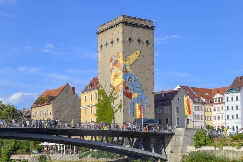 A bridge with a colorful mural on a tower, surrounded by historic buildings. 3