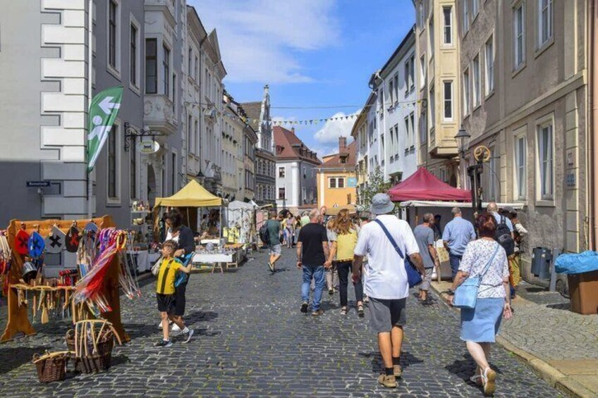 A cobblestone street with people walking, market stalls, and buildings. 4