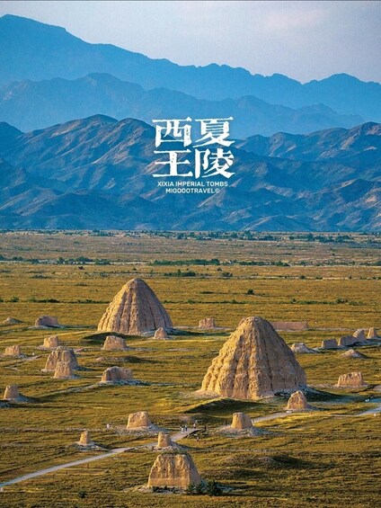 A landscape with large, rounded rock formations in a grassy field, with mountains in the background. 1