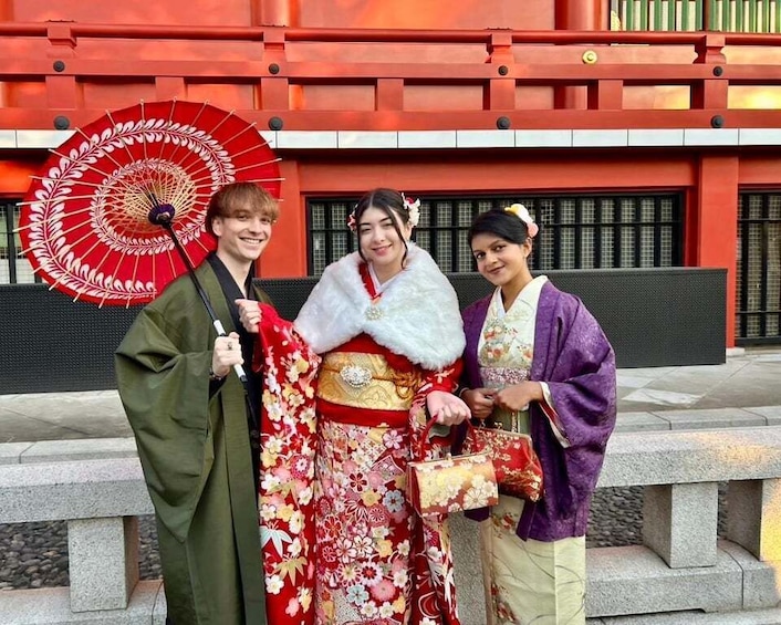 Three people in traditional Japanese attire, a red fan, and a red building with a white railing. 3