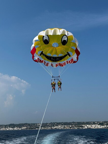 Two people parasailing with a smiling face parachute over the ocean. 3