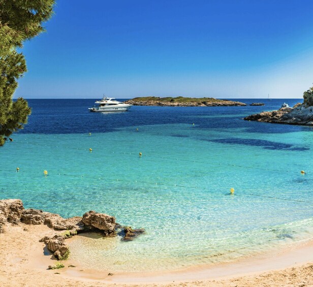 A clear turquoise sea, a sandy beach, rocky outcrops, and a boat anchored in the distance. 3
