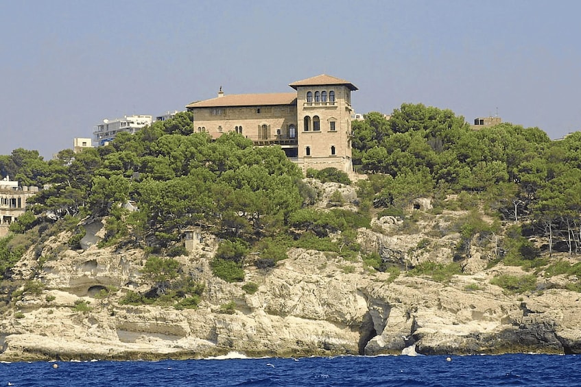 A coastal building with a tower, surrounded by rocky terrain and dense greenery. 2