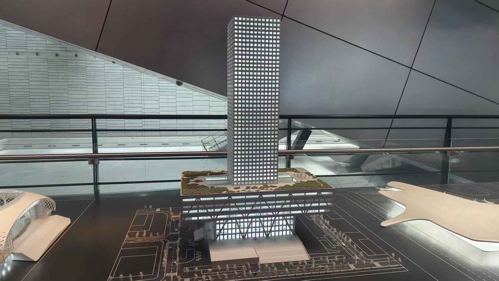 A model of a modern high-rise building with a grid of windows, surrounded by a spacious area with a ramp and a small bridge. 3