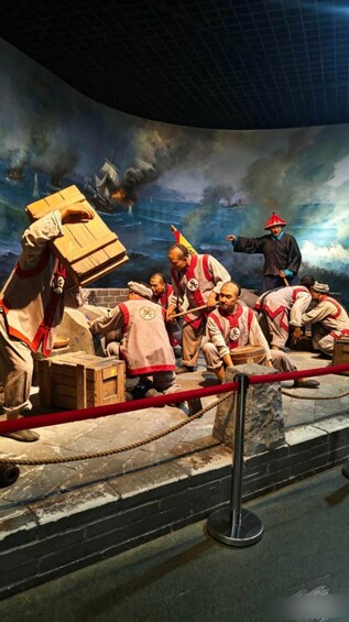 A historical reenactment scene with people in period costumes, wooden crates, and a backdrop depicting a ship and smoke. 5