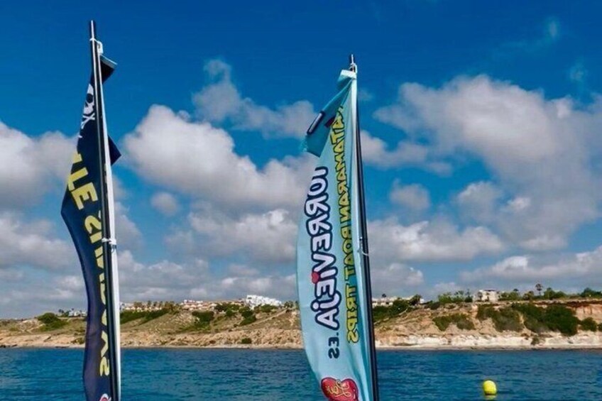 Two flags with text, a clear blue sky, and a coastline with buildings in the background. 2