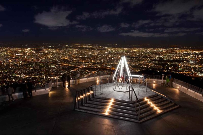 A nighttime cityscape with a prominent light sculpture in the foreground. 3