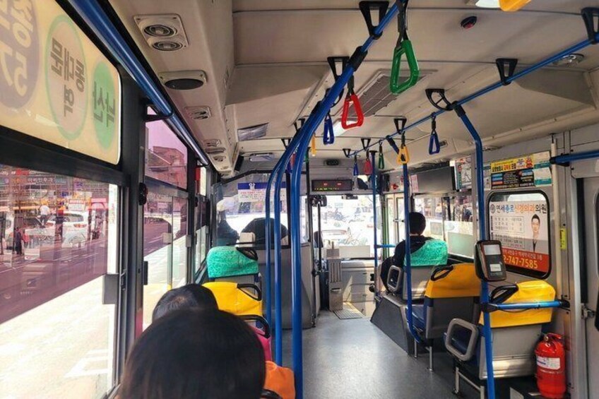 The interior of a bus with yellow seats, blue handrails, and a digital display. 2