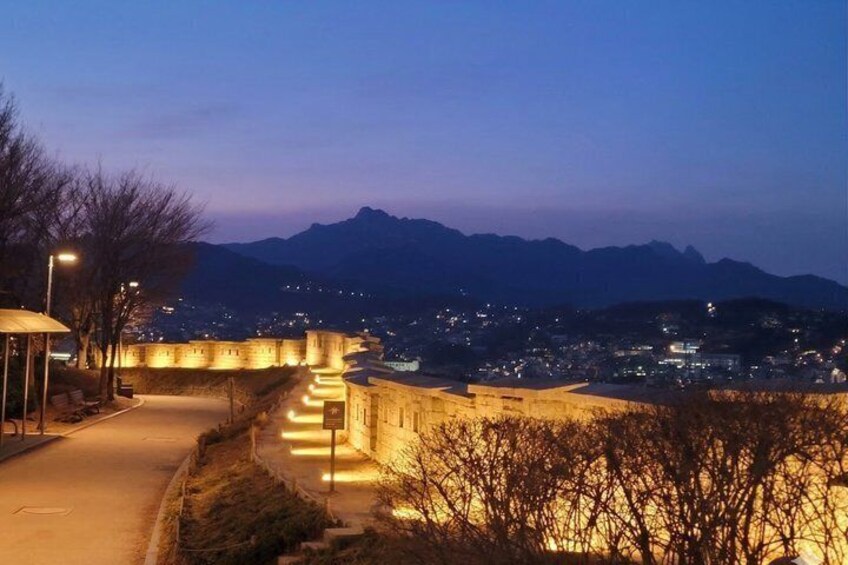 A well-lit pathway leading to a historic fortification overlooking a city at dusk. 4
