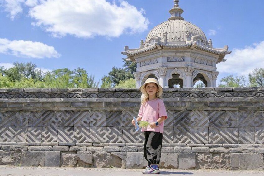 A person standing in front of a patterned stone wall with a pagoda-like structure in the background. 1