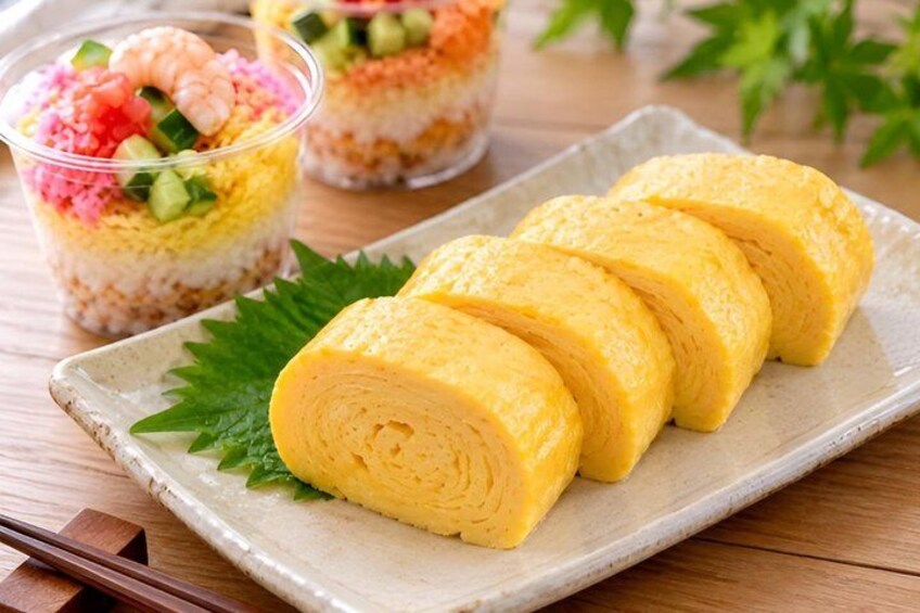 A plate with rolled omelette slices and a container of layered dessert with shrimp and vegetables. 2