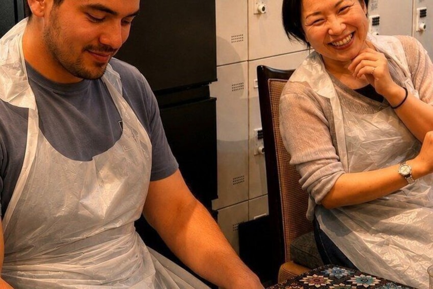 Two people wearing aprons, one seated and one standing, in a room with lockers in the background. 4