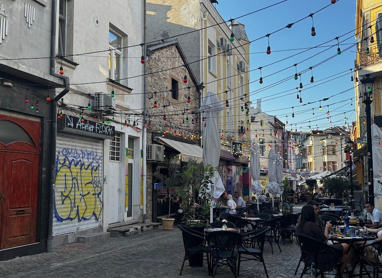 A cobblestone street with outdoor seating, buildings with signage, and string lights. 4