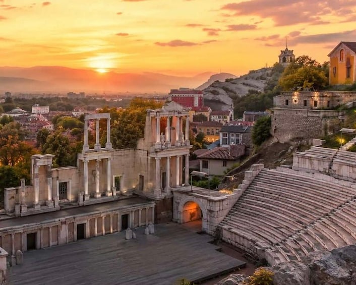 An ancient amphitheater with ruins and classical architecture, set against a sunset sky. 1