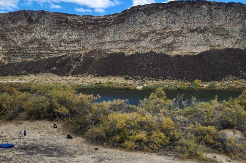 A desert landscape with a large rock formation, sparse vegetation, and a small body of water. 1