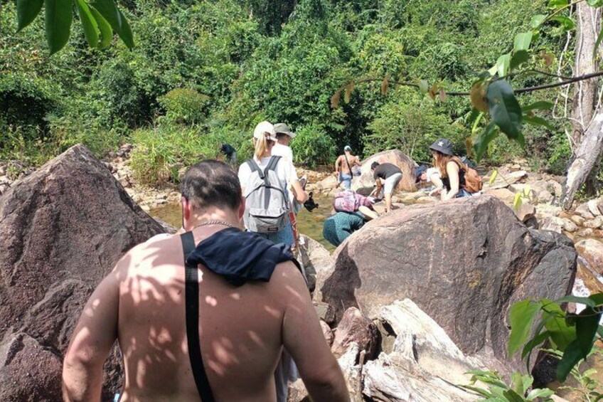 A group of people hiking in a forested area with large rocks and a river. 4