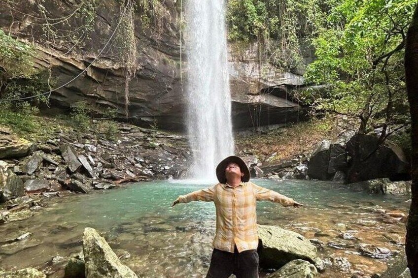 A waterfall, rocky terrain, and a person standing in a shallow stream. 3