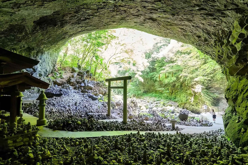 A cave entrance with a stone torii gate, a pathway, and lush greenery. 3