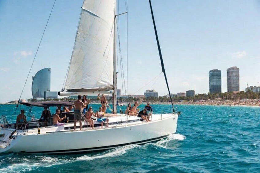 A sailboat with people on board, a beach, and buildings in the background. 2