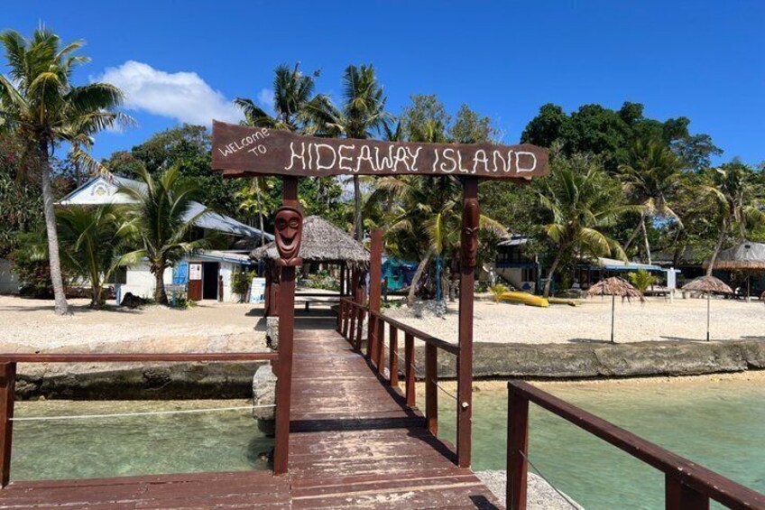 A wooden pier leading to a beach with palm trees and a sign that reads 'Welcome to Hideaway Island.' 1