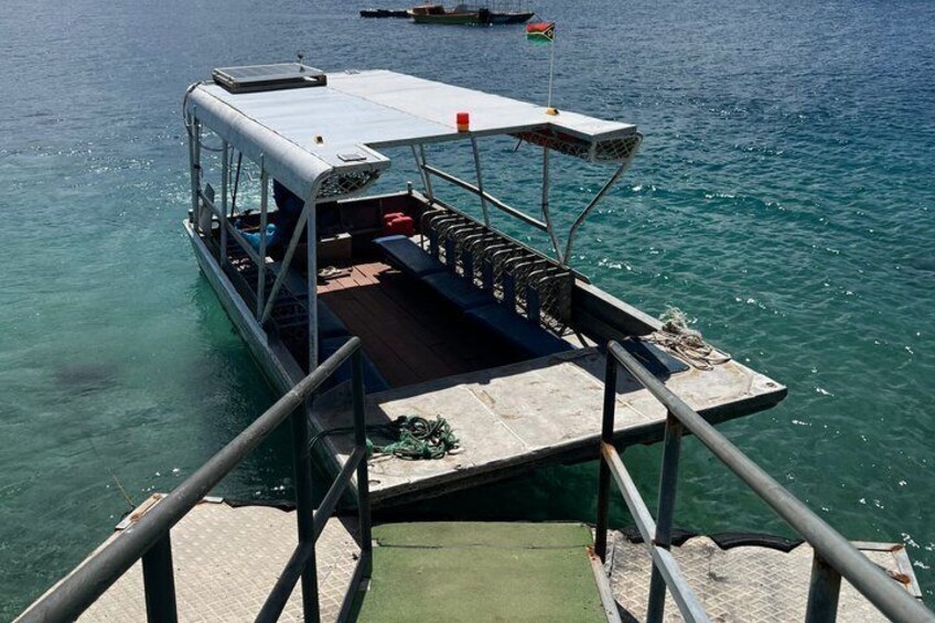A boat docked at a pier with a covered deck area, a small flag, and a clear blue water background. 2