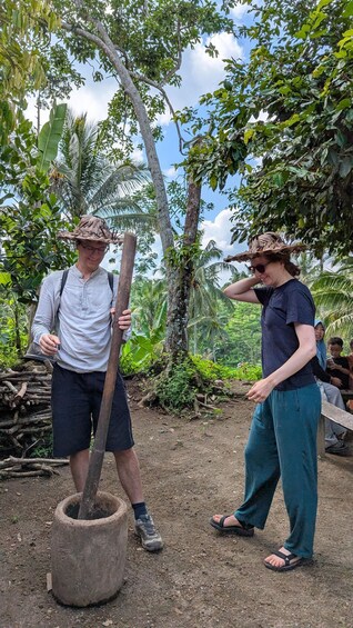 Two people in a tropical forest, one holding a stick, and another wearing a hat. 4