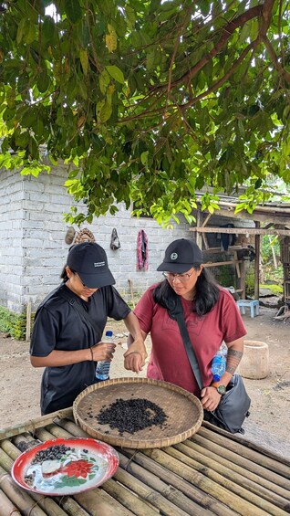 Two people preparing food outdoors, with a basket of black beans and a plate of spices. 3