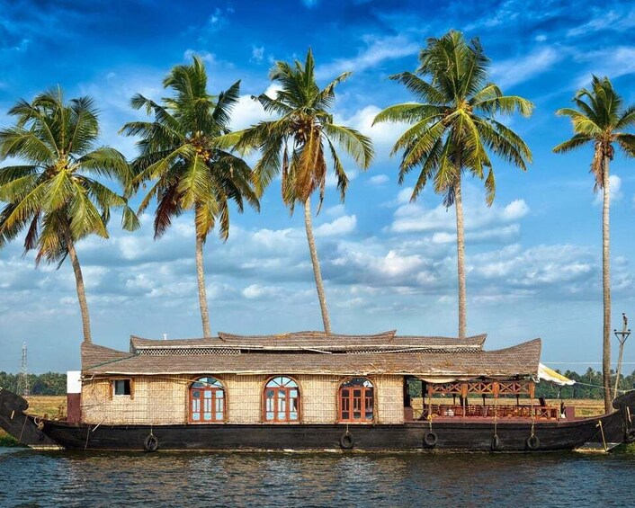 A traditional houseboat with a tiled roof and wooden walls, floating on water with palm trees in the background. 1