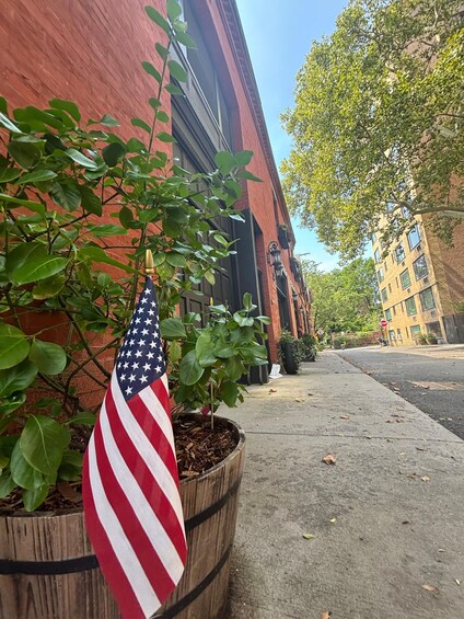 A street with a red brick building, a wooden planter with an American flag, and a sidewalk. 4