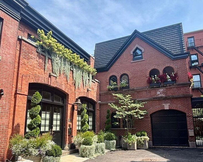 A red brick building with a black garage door, a small window, and a tree in the front yard. 1