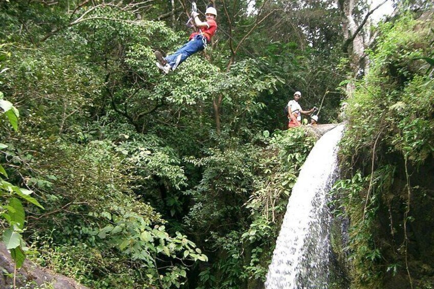 A person zip-lining through a forested area with a waterfall. 4